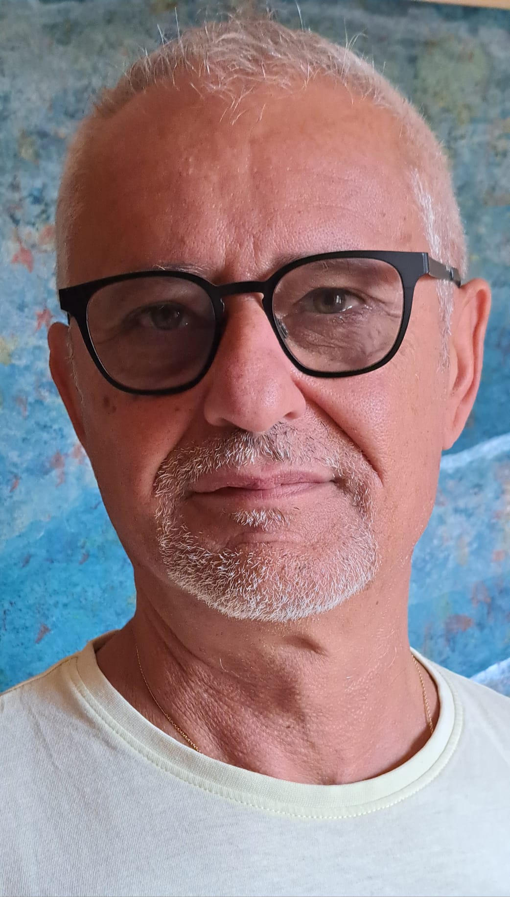 Close-up portrait of Giancarlo Carnevale wearing black glasses, in front of a blue painting.